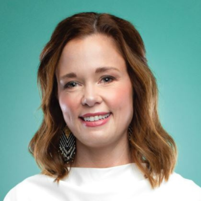 Amanda Logue smiles for headshot wearing a white blouse, in front of a teal background