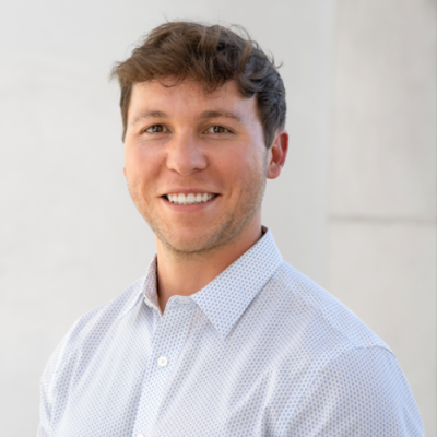 Hunter Thevis smiles for headshot in front of a blank wall wearing a powder blue button-up shirt