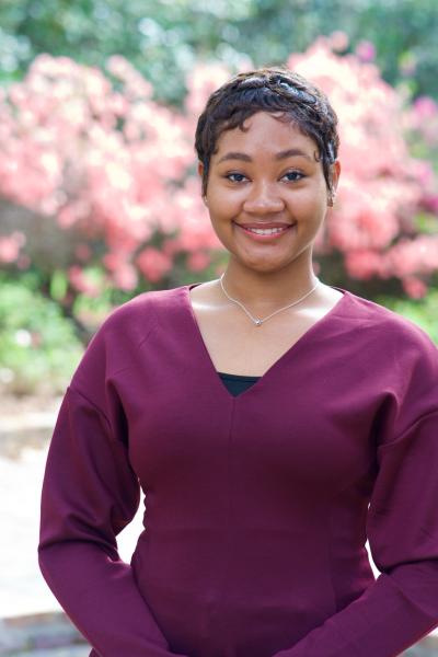Smiling headshot of Jordyn in a burgundy sweater with pink flowers in the background