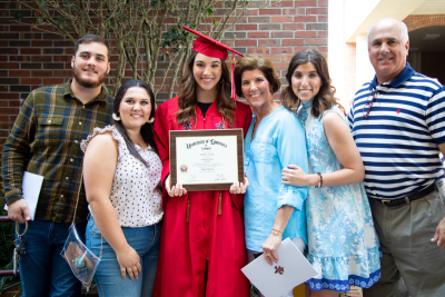 Online bachelor's degree grad smiles with family, wearing a red UL Lafayette cap and gown.