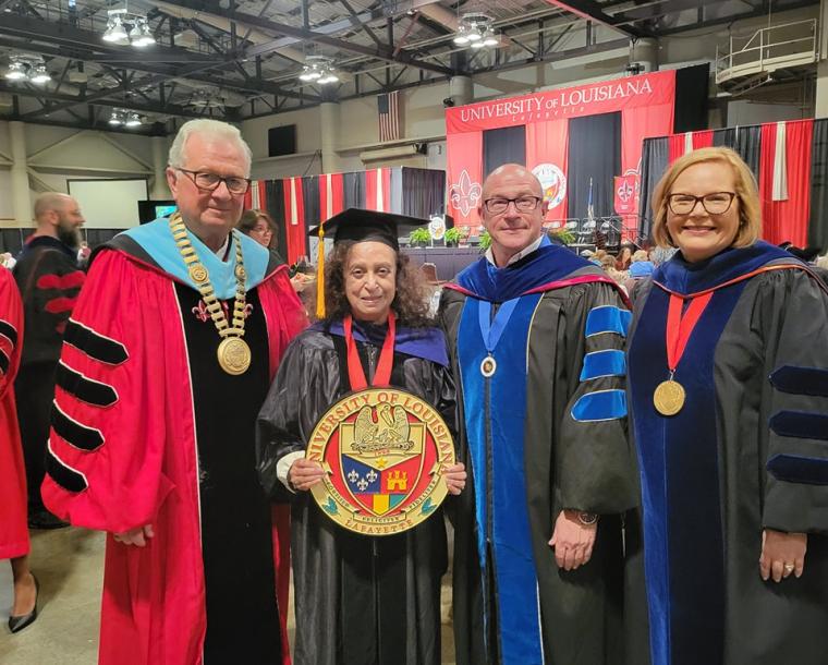 Dr. Vatsala posing with the university seal with Dean Farmer-Kaiser, Dr. Savoie, and Dr. Hebert