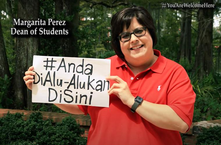 Margarita Perez, Dean of Students, holding up a white sign that says # Anda Di Alu-Alukai Di Sini to welcome UL Lafayette international students.