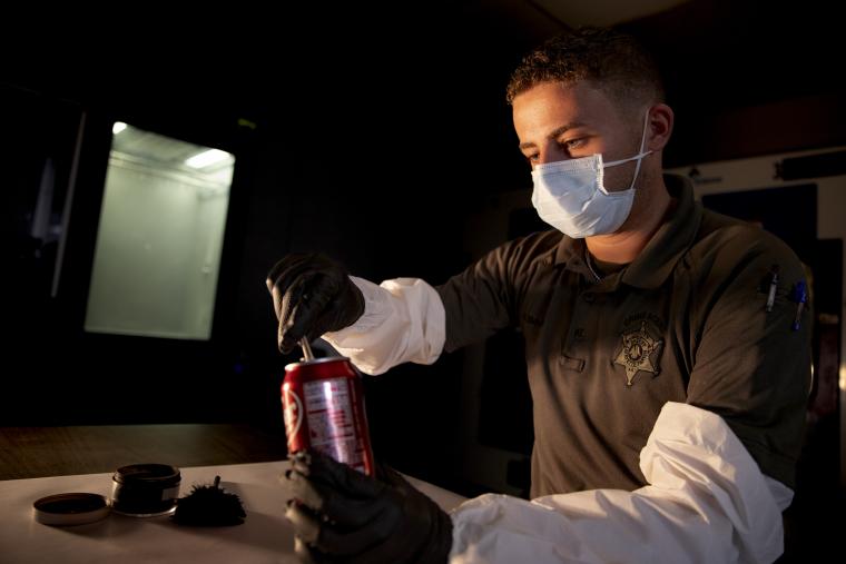 Criminal Justice alumni collects evidence from a soda can in his role as a detective with the police department