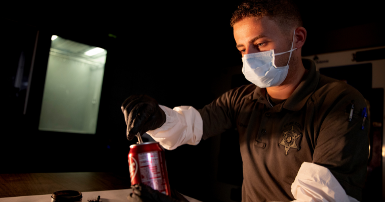 Criminal Justice alumni collects evidence from a soda can in his role as a detective with the police department