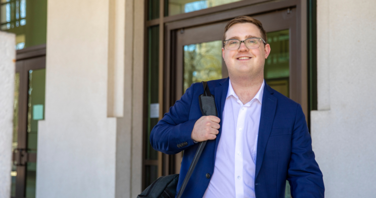 Zack Schleter smiles while walking out of a courthouse, wearing a blazer and work bag.