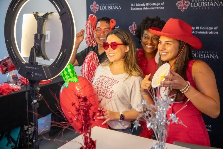 Students holding red props pose in front of a B.I. Moody III College of Business Administration backdrop 