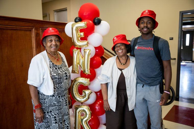 A student and his family wear red College of Engineering hats and pose near an ENGR balloon display