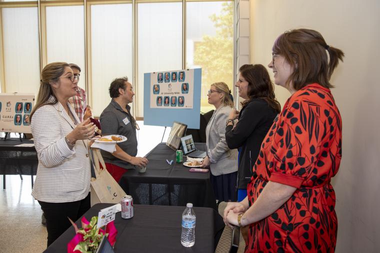 FLC Showcase presenters and attendees are pictured standing on either side of tables as presenters answer questions regarding FLC deliverables.
