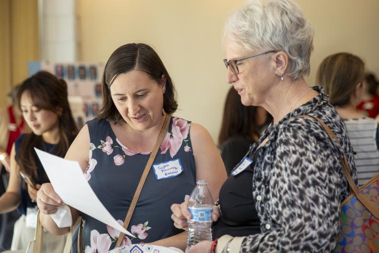 Two women attending the FLC Showcase are pictured reviewing a handout from one of the FLC presenters.
