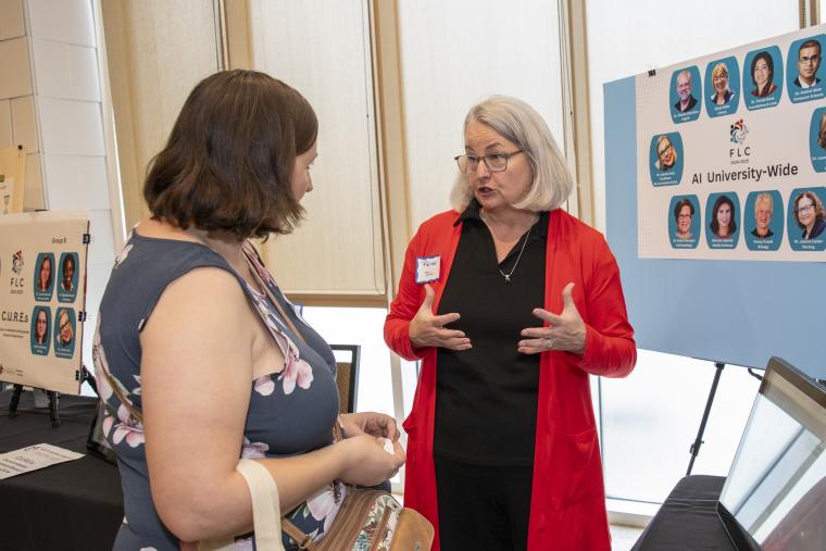 Instructional Technologist Renee Fiser is pictured in front of a research poster presentation as she speaks to a woman attending the FLC Showcase.