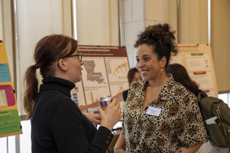Two women speak facing each other with research poster presentations in the background during the 2025 FLC Showcase.