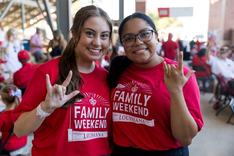 Two students wearing Family Weekend t-shirts pose and display the UL hand sign