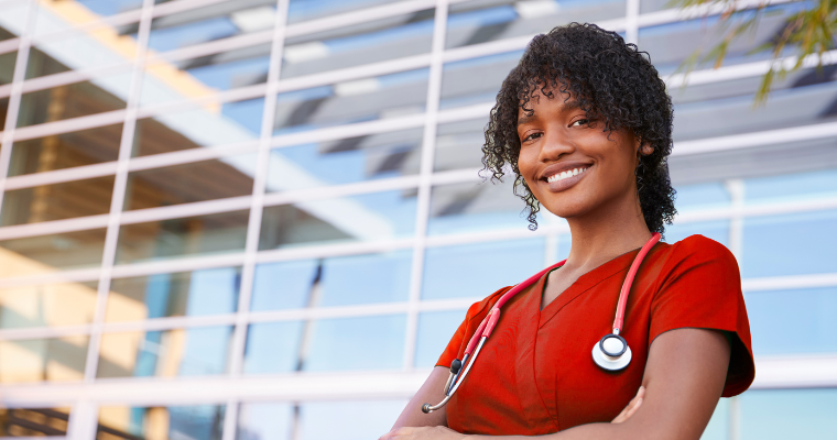 Nurse in red scrubs smiles with arms crossed.