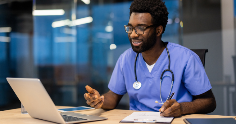 RN to BSN online student studies on a laptop wearing blue scrubs and a stethoscope.