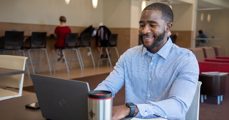 UL Lafayette online Finance MBA student studies on campus wearing a blue collared shirt.