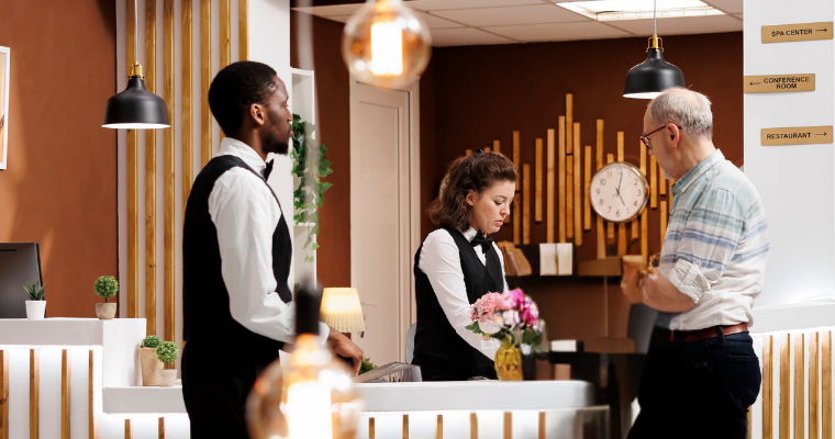 Two hospitality managers wearing formal work attire attend to a customer in a hotel lobby.