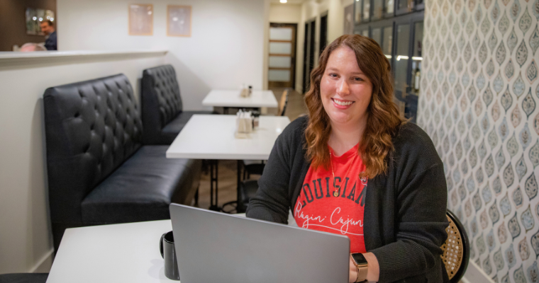 Sarah Monroe smiles in a local restaurant wearing a red Ragin' Cajun t-shirt and black blazer.