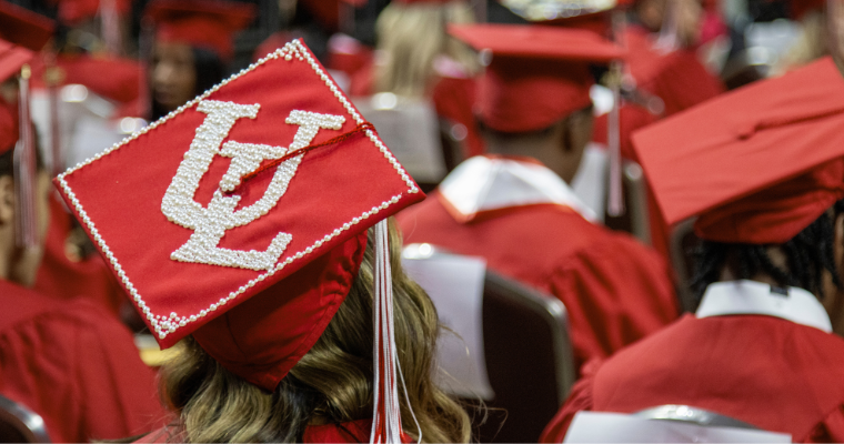 Online bachelor's degree grad wears a red cap with UL Lafayette's emblem bedazzled on it. 