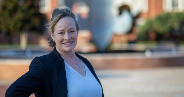 Melissa Malik, online enrollment specialist at UL Lafayette, smiles for a portrait in front of the fleur-de-lis fountain on UL Lafayette's campus.