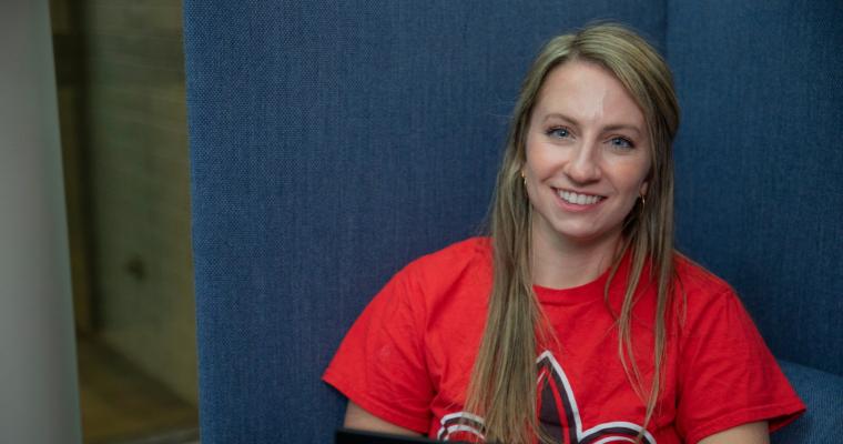 Student works on their online graduate degree in a sitting booth, wearing a red Ragin' Cajuns shirt.