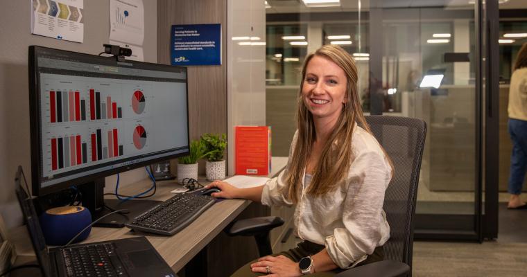 Alumna of the online informatics degree program smiles as she works at a desktop in an office setting.
