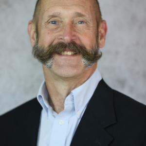 Portrait photograph of Dr. Mark Smith smiling wearing a blue button down shirt and a black blazer.