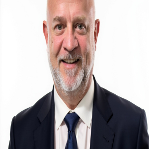 Portrait photograph of David Baker smiling wearing a white button down shirt, a blue tie, and a black blazer.