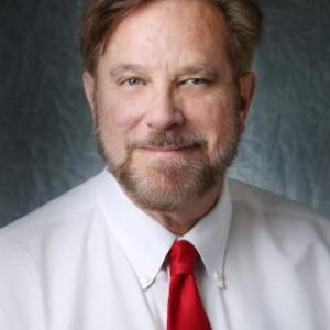 Portrait photo of Fred Davis smiling and wearing a white button down shirt with a red tie.