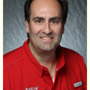 Portrait photograph of Tim McCoy smiling and wearing a red Ragin' Cajuns logo shirt.
