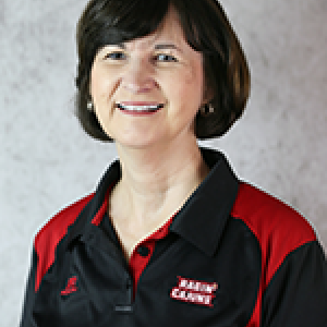 Portrait photo of Julie McNulty smiling and wearing a black and red Ragin' Cajuns logo polo shirt.
