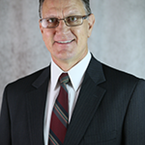 Portrait photo of David Stevens smiling wearing glasses, a white button down shirt, a red sequences tie, and a black blazer.