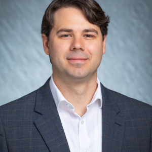 Portrait photograph of Alex Slepchuk smiling and wearing white button down and blue blazer.