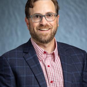 Portrait photo of Josh Bendickson smiling in a red button and black blazer