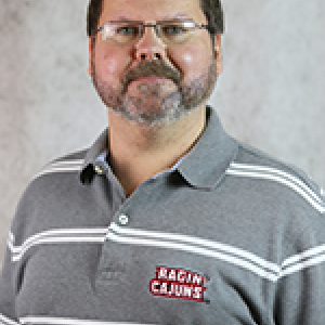 Portrait photograph of Wes Austin in a grey and white striped Ragin Cajuns polo shirt.