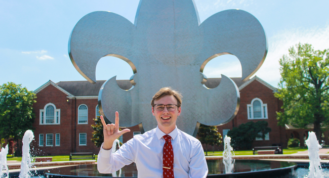 University of Louisiana at Lafayette education major Dylan Hebert in front of the iconic fleur de lis fountain in the campus quad