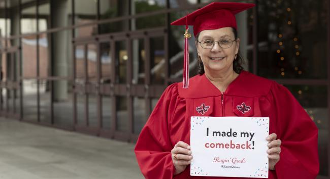 Karen LeDoux, wearing her cap and gown, holds up a sign that reads, "I made my comeback!"
