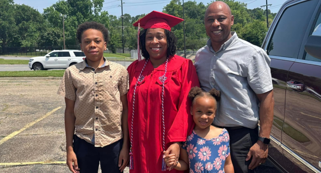 RN to BSN grad Tiffany Woods smiles for photo with husband, son, and daughter in her cap and gown.