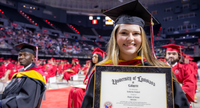 MS in Informatics graduate wearing a black cap and gown smiles with diploma at UL Lafayette commencement ceremony
