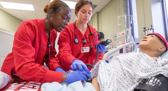 Two nursing students participate in a simulation lab.