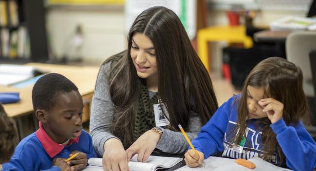 An education student helps two elementary students in their classroom.