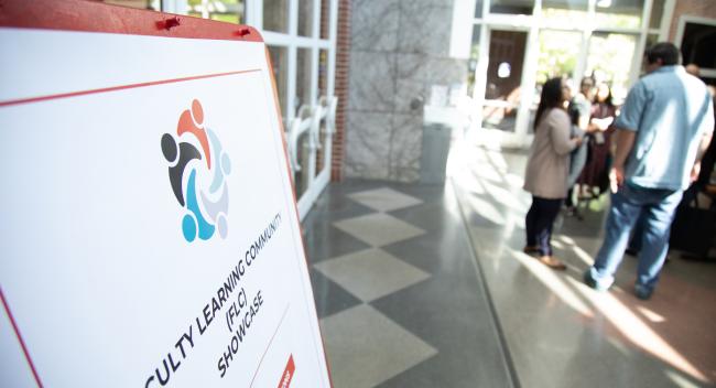 A sign for the Faculty Learning Community Showcase is pictured in the foreground with participants seen milling in the background.