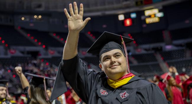 Mason Blanchard, wearing his master's regalia, waves up at his family after having his M.S. in Systems Technology degree conferred.