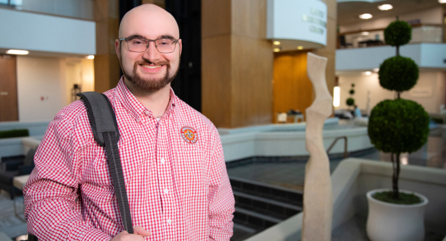 Online M.S. in Accounting alumni Seth Prather smiles in an office setting, wearing a red UL Lafayette button-down and shoulder bag.
