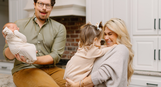 Online MBA grad Victoria Alleman smiles in kitchen with her babies and husband.