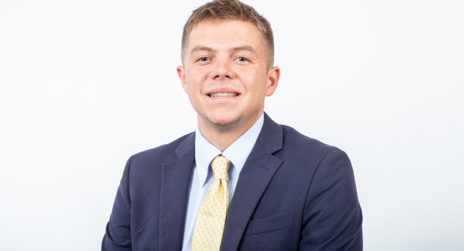 William Fralia, alumnus of the University of Louisiana at Lafayette's sport management program, smiles for a headshot in a suit.
