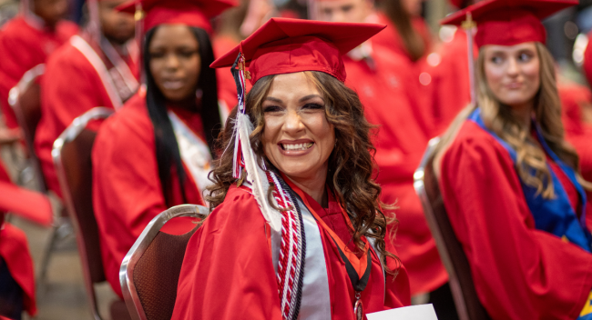 Online General Studies graduate smiles in cap and gown while seated at UL Lafayette's commencement ceremony.