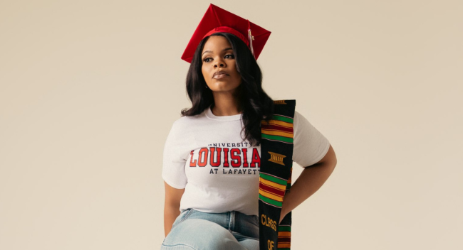Chanoah Smith poses for photo wearing a white UL Lafayette t-shirt and red graduation cap after completing the management degree online program.