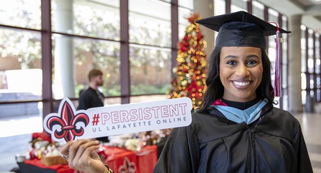 Graduate of the online Master of Education program smiles at commencement while holding a sign that reads "#Persistent"