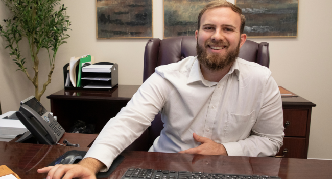 Dylan Chesterman, graduate of UL Lafayette's online master's in accounting, smiles while crunching numbers at his desk.