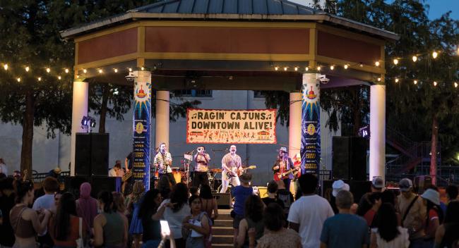A band performs on an outdoor stage with people watching in the foreground.